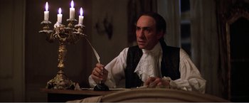 Movie still from “Amadeus” (1984), directed by Milos Forman – A man holding a knife in front of a lit candle; Medium shot, Over the shoulder angle