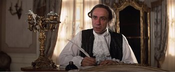 Movie still from “Amadeus” (1984), directed by Milos Forman – A man sitting at a table with a feather in his hand; Medium shot, Low angle