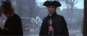 Movie still from “Amadeus” (1984), directed by Milos Forman – A man in a black coat and a hat holding a pipe; Medium shot, Over the shoulder angle
