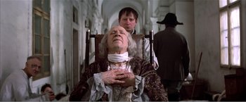 Movie still from “Amadeus” (1984), directed by Milos Forman – An old man sitting in a chair in front of a young man; Medium shot, Low angle