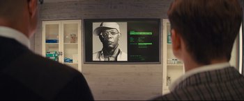 Movie still from “Kingsman: The Secret Service” (2014), directed by Matthew Vaughn – A man wearing a hat and glasses in front of a television; Close Up shot, Over the shoulder angle