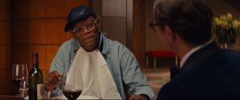 Movie still from “Kingsman: The Secret Service” (2014), directed by Matthew Vaughn – A man sitting at a table in front of a glass of red wine; Close Up shot, Over the shoulder angle