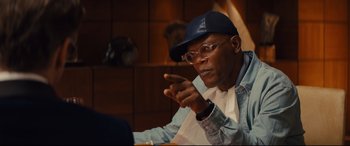 Movie still from “Kingsman: The Secret Service” (2014), directed by Matthew Vaughn – A man wearing glasses and a hat is sitting at a table; Close Up shot, Over the shoulder angle