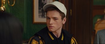 Movie still from “Kingsman: The Secret Service” (2014), directed by Matthew Vaughn – A young man wearing a baseball cap looking to his left; Close Up shot, Over the shoulder angle