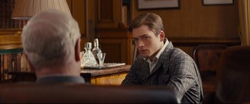 Movie still from “Kingsman: The Secret Service” (2014), directed by Matthew Vaughn – A man sitting in front of another man in front of a mirror; Medium shot, Over the shoulder angle
