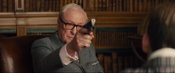 Movie still from “Kingsman: The Secret Service” (2014), directed by Matthew Vaughn – An older man holding a gun in a library; Close Up shot, Over the shoulder angle