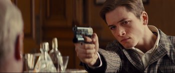Movie still from “Kingsman: The Secret Service” (2014), directed by Matthew Vaughn – A man holding a gun in his right hand; Close Up shot, Low angle