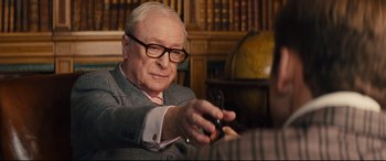 Movie still from “Kingsman: The Secret Service” (2014), directed by Matthew Vaughn – An older man in a suit and glasses looking at a cell phone; Close Up shot, Over the shoulder angle