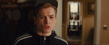 Movie still from “Kingsman: The Secret Service” (2014), directed by Matthew Vaughn – A young man wearing a baseball cap and a black jacket; Close Up shot, Over the shoulder angle
