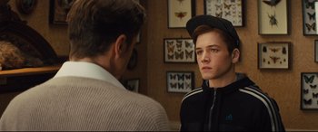 Movie still from “Kingsman: The Secret Service” (2014), directed by Matthew Vaughn – A young man is looking at another young man in front of a wall of butterflies; Close Up shot, Over the shoulder angle