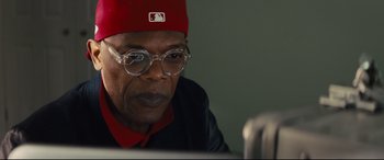 Movie still from “Kingsman: The Secret Service” (2014), directed by Matthew Vaughn – An older man wearing glasses and a red hat; Close Up shot, Over the shoulder angle