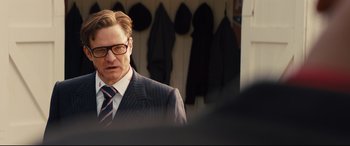 Movie still from “Kingsman: The Secret Service” (2014), directed by Matthew Vaughn – A man in a suit and tie standing in front of jackets; Close Up shot, Over the shoulder angle
