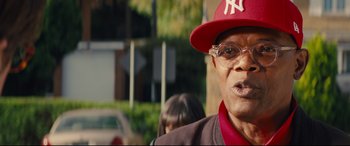 Movie still from “Kingsman: The Secret Service” (2014), directed by Matthew Vaughn – An older man wearing glasses and a red hat; Close Up shot, Over the shoulder angle