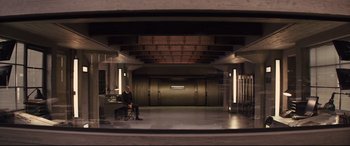 Movie still from “Kingsman: The Secret Service” (2014), directed by Matthew Vaughn – A man sitting at a desk in a room; Wide shot, High angle