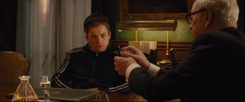 Movie still from “Kingsman: The Secret Service” (2014), directed by Matthew Vaughn – A man sitting in front of a mirror holding a cigarette; Medium shot, Over the shoulder angle