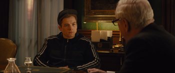 Movie still from “Kingsman: The Secret Service” (2014), directed by Matthew Vaughn – A man sitting in front of another man in front of a painting; Medium shot, Over the shoulder angle