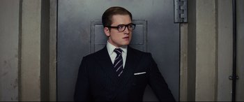 Movie still from “Kingsman: The Secret Service” (2014), directed by Matthew Vaughn – A man wearing a suit and tie standing in front of a wall; Close Up shot, Low angle