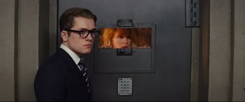 Movie still from “Kingsman: The Secret Service” (2014), directed by Matthew Vaughn – A man standing next to a woman in a jail cell; Medium shot, Over the shoulder angle