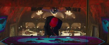 Movie still from “Kingsman: The Secret Service” (2014), directed by Matthew Vaughn – A man wearing a red hat is looking down at a table; Wide shot, High angle