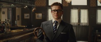 Movie still from “Kingsman: The Secret Service” (2014), directed by Matthew Vaughn – A man in a suit and tie holding a cane; Medium shot, Low angle