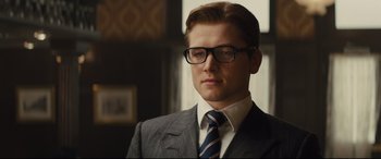 Movie still from “Kingsman: The Secret Service” (2014), directed by Matthew Vaughn – A man in a suit and tie wearing glasses; Close Up shot, Low angle