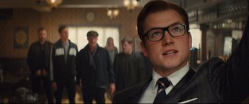 Movie still from “Kingsman: The Secret Service” (2014), directed by Matthew Vaughn – A group of people in a room with a man in a suit; Close Up shot, Low angle