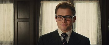Movie still from “Kingsman: The Secret Service” (2014), directed by Matthew Vaughn – A man in a suit and tie wearing glasses; Close Up shot, Over the shoulder angle