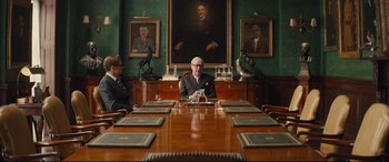 Movie still from “Kingsman: The Secret Service” (2014), directed by Matthew Vaughn – A man sitting at a table in front of two other men; Wide shot, Low angle