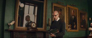 Movie still from “Kingsman: The Secret Service” (2014), directed by Matthew Vaughn – A bald man in a suit and tie looking at a book; Medium shot, Low angle