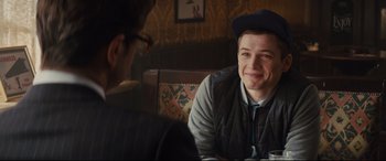 Movie still from “Kingsman: The Secret Service” (2014), directed by Matthew Vaughn – A man sitting in front of another man at a table; Close Up shot, Over the shoulder angle