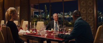 Movie still from “Kingsman: The Secret Service” (2014), directed by Matthew Vaughn – A man sitting at a dinner table with two other people; Medium shot, Over the shoulder angle