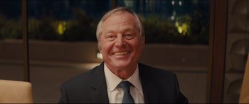 Movie still from “Kingsman: The Secret Service” (2014), directed by Matthew Vaughn – An older man wearing a suit and tie smiling; Close Up shot, Over the shoulder angle
