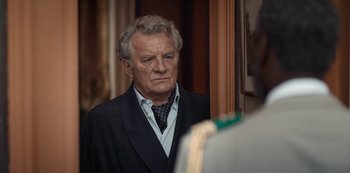 Movie still from “Lupin” (2021), created by Tigran Rosine – An older man wearing a suit and tie looking out a window; Close Up shot, Over the shoulder angle