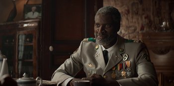 Movie still from “Lupin” (2021), created by Tigran Rosine – An older man in a military uniform sitting at a table; Medium shot, Over the shoulder angle