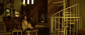 Movie still from “Magic Mike” (2012), directed by Steven Soderbergh – A woman sitting on top of an ottoman in a living room; Wide shot, Low angle