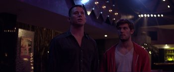 Movie still from “Magic Mike” (2012), directed by Steven Soderbergh – Two men standing next to each other in front of lights; Medium shot, Low angle