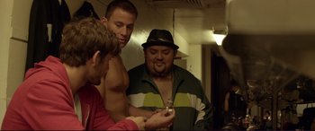Movie still from “Magic Mike” (2012), directed by Steven Soderbergh – A group of men looking at a cell phone in a room; Medium shot, Over the shoulder angle