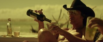 Movie still from “Magic Mike” (2012), directed by Steven Soderbergh – A man sitting on the beach holding a bottle of wine and a glass; Medium shot, Low angle