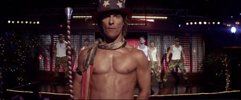 Movie still from “Magic Mike” (2012), directed by Steven Soderbergh – A man in a patriotic hat is posing in front of a group of men; Medium shot, Over the shoulder angle