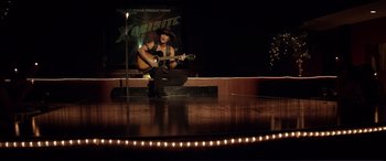 Movie still from “Magic Mike” (2012), directed by Steven Soderbergh – A man sitting on a stage with a guitar; Wide shot, Over the shoulder angle