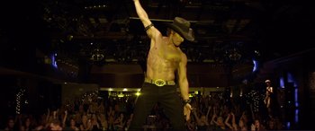 Movie still from “Magic Mike” (2012), directed by Steven Soderbergh – A man in a cowboy hat is performing on a stage; Medium shot, High angle