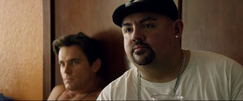 Movie still from “Magic Mike XXL” (2015), directed by Gregory Jacobs – A man with a beard wearing a black hat and a white shirt; Close Up shot, Over the shoulder angle