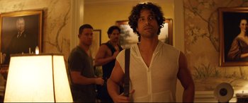 Movie still from “Magic Mike XXL” (2015), directed by Gregory Jacobs – A man holding a bag in front of two other men; Medium shot, Over the shoulder angle