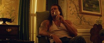 Movie still from “Magic Mike XXL” (2015), directed by Gregory Jacobs – A man sitting in a chair holding a wine glass; Medium shot, Low angle