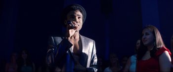Movie still from “Magic Mike XXL” (2015), directed by Gregory Jacobs – A man in a silver jacket is holding a microphone; Medium shot, Over the shoulder angle