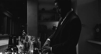 Movie still from “Malcolm & Marie” (2021), directed by Sam Levinson – A black and white photo of a man standing in front of a counter; Medium shot, Low angle