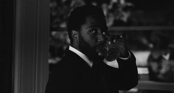 Movie still from “Malcolm & Marie” (2021), directed by Sam Levinson – A black and white photo of a man in a suit drinking a glass; Close Up shot, Low angle