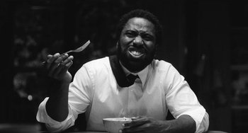 Movie still from “Malcolm & Marie” (2021), directed by Sam Levinson – A black and white photo of a man holding a knife and a bowl; Close Up shot, Low angle