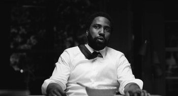 Movie still from “Malcolm & Marie” (2021), directed by Sam Levinson – A black and white photo of a man sitting at a table with a bowl; Close Up shot, Low angle