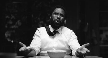 Movie still from “Malcolm & Marie” (2021), directed by Sam Levinson – A black and white photo of a man sitting at a table with a bowl; Close Up shot, Low angle